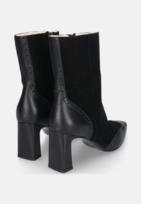 Zwarte enkellaarsjes met een combinatie van suede en leer. Vierkante neus, blokhak en decoratieve stiksels langs de naden.