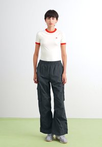 T-shirt blanc avec bord rouge et logo, associé à un pantalon cargo noir ample avec poches latérales et ceinture élastique.