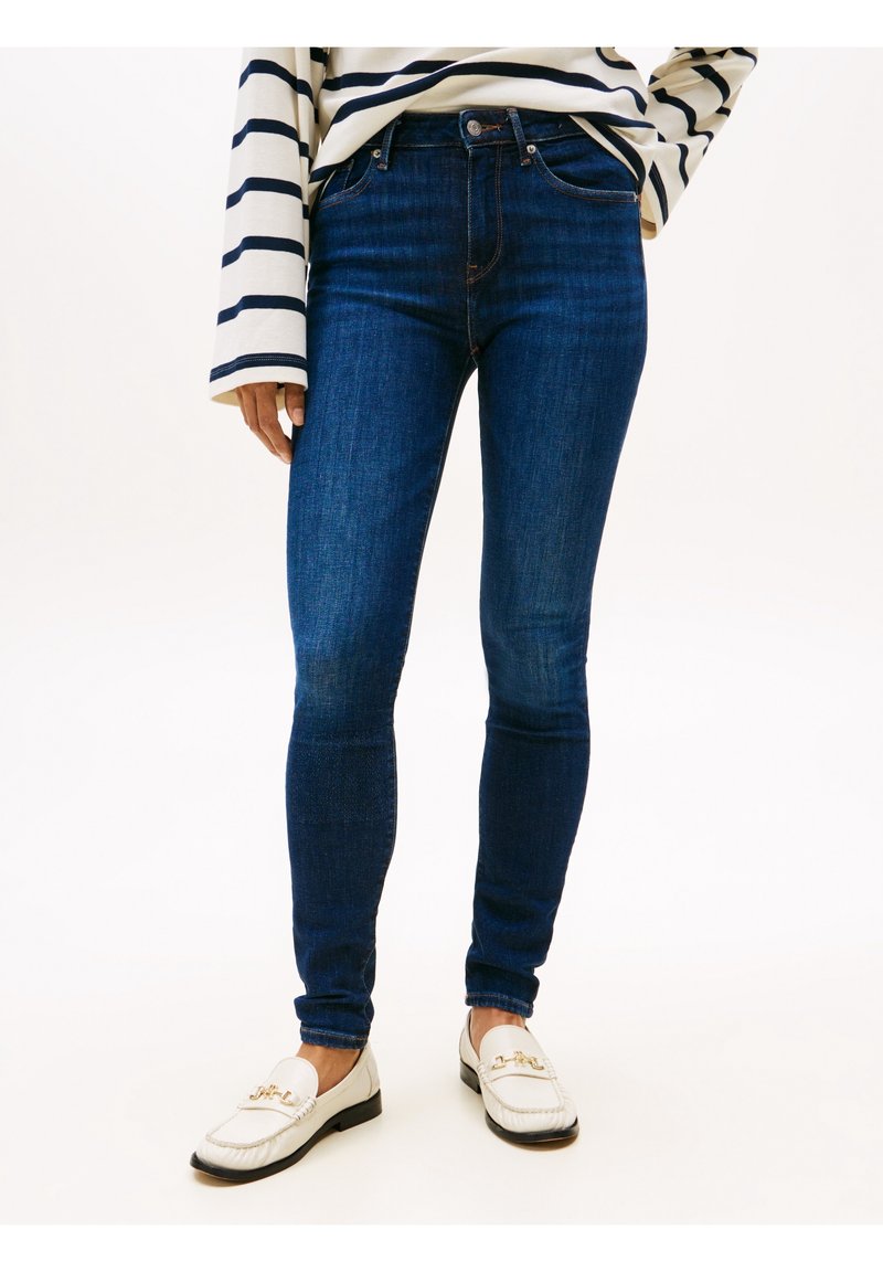 Smala blå denimjeans med hög midja och fin struktur, tillsammans med en vit topp med marinblå horisontella ränder och vita loafers.