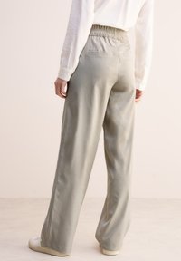 Pantaloni a gamba larga grigio chiaro realizzati in un tessuto morbido, dotati di una vita elasticizzata e due tasche posteriori, con un design minimalista.