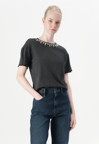 Tricou negru cu mânecă scurtă, decorat cu mărgele în jurul gulerului, asortat cu blugi de denim închis, cu talie înaltă.