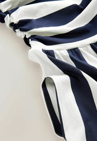 Marinblå och vit randig tyg med rynkade elastiska detaljer, mjuk textur och kontrasterande kanter. Har flödande draperingar och sidöppningar.