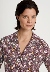 Bloemmotief shirt in paarse tinten met groene en gele accenten. Heeft een kraag en korte mouwen. Soepele stoftextuur.