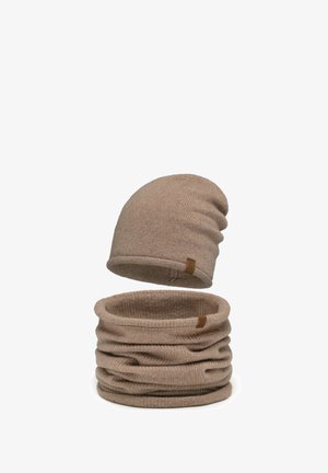 Bonnet d'hiver en tricot beige et tour de cou assorti avec petites étiquettes de marque marron, tous deux doux et texturés.