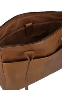 Bruine leren tas met een ritssluiting, binnenzak en een gladde textuur. Kenmerkt subtiele merkidentificatie die binnenin is gebosseleerd.