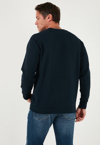 Tengerészkék pulóver puha anyagból, hosszú ujjakkal, bordázott mandzsettákkal és szegéllyel, lekerekített nyakkivágással és laza hátrésszel.