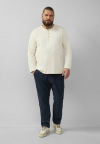 Lichtbeige langeknops-henley shirt met drie knopen, gecombineerd met marineblauwe broeken en beige sneakers. Eenvoudig, comfortabel ontwerp.