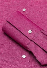Fuchsia Hemd mit strukturiertem Gewebe, ausgestattet mit umgeschlagenen Ärmeln, weißen Knöpfen und einer taillierten Passform, die ein dezentes Muster zeigt.