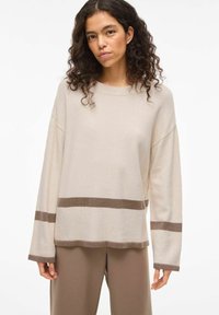 Pull beige à col rond, manches longues, avec des rayures horizontales marron à l'ourlet et aux manches. Texture douce, coupe décontractée.