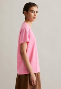 Rosa Baumwoll-T-Shirt mit kurzen Ärmeln und lässigem Schnitt, mit rundem Ausschnitt und weicher Textur. Das Model trägt einen braunen Rock.