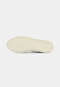 Gummisål med en bølgemønster, overvejende off-white farve, med teksturerede greb langs kanterne for bedre trækkraft.