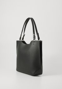 Black leather tote bag with textured surface, two adjustable straps, large interior, and a flat exterior pocket. Geometric shape with minimal detailing.