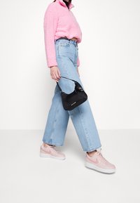 Borsa nera a forma curva con manico corto, indossata con un pullover rosa peloso e jeans a gamba larga azzurri, abbinata a sneaker rosa.