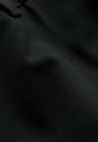 Sort stof med en glat tekstur og subtil stræk. Har bløde folder og en let glans, der fremhæver et minimalistisk design.