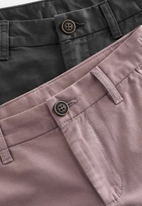 Deux paires de pantalons, une en gris foncé et l'autre en rose pâle. Les deux présentent des ceintures plates avec des fermetures à bouton et des détails de couture assortis.