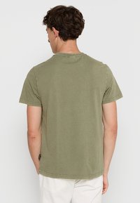 Olivengrøn bomulds t-shirt, kortærmet, rund halsudskæring, med en afslappet pasform og synlige sømdetaljer langs kanten og ærmerne.