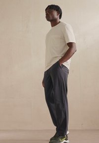 Helles graues Kurzarm-T-Shirt mit Tasche, kombiniert mit dunkelgrauen Hosen und grünen Nike-Sneakern. Glattes Material und entspannter Sitz.