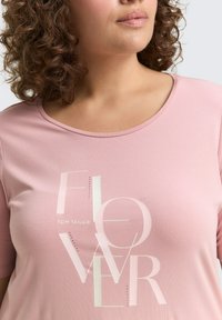 Rosa T-shirt met een ronde hals, korte mouwen en een decoratieve "FLOWER" grafiek met subtiele versieringen.
