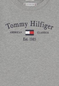 Gray cotton T-shirt featuring embroidered "Tommy Hilfiger" text, a horizontal color block in red, white, and blue, and "Est. 1985."