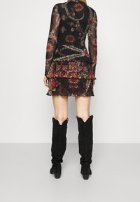 Robe fleurie noire à manches longues avec ourlet à volants, en tissu transparent, ornée de motifs colorés. Associée à des bottes noires montantes jusqu'aux genoux.