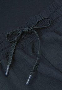 Mörkblå elastisk midja med snörning. Snörningen har texturerade ändar och är vävd i tyget, vilket ger ett glatt utseende.