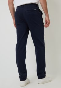 Pantalones azul marino de algodón con corte recto, que cuentan con dos bolsillos traseros y una cintura elástica, combinados con zapatillas blancas.