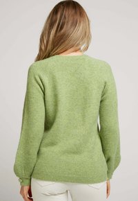 Pull en laine vert présentant une texture douce, un col rond et de longues manches raglan avec des accents de boutons aux poignets.