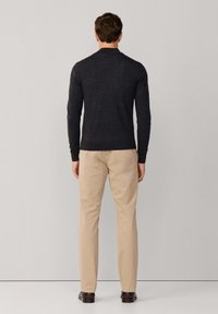 Donkergroot grijs lange mouwen trui gemaakt van knit stof, gecombineerd met lichtbeige broeken, afgebeeld vanachter tegen een neutrale achtergrond.