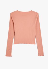 Geribbelde lange mouw top in stofroze, met een ronde hals en een onafgewerkte zoom met gekruiste randen. De stof is zacht en heeft een zichtbare textuur.