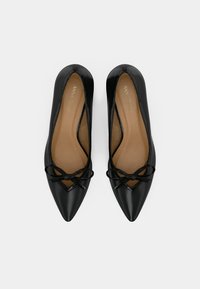 Ζευγάρι μαύρων μπαλαρινών με μυτερή μύτη και μικρές κορδέλες μπροστά, μπεζ εσωτερικά πέλματα και τυπωμένο "ANNA FIELD" στο εσωτερικό.