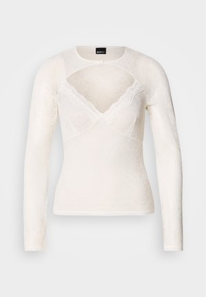 Hvit langermet topp laget av blonder med V-hals og delikat blonderkant langs halsen. Har knappelukking ved kragen.