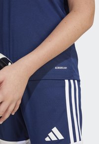 Maillot de sport bleu marine avec des rayures blanches et le logo "AEROREADY", fabriqué en matériau synthétique texturé, porté avec un ballon de football noir et blanc.