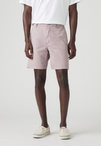 Pantaloni scurți pentru bărbați, de culoare roz deschis, cu o croială clasică, confecționați dintr-un material țesut. Au buzunare frontale și un design plat în față. Asortați cu adidași albi.
