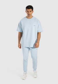 T-shirt oversize di cotone blu chiaro abbinato a pantaloni tuta coordinati. Texture liscia, maniche corte, logo minimale sul petto.