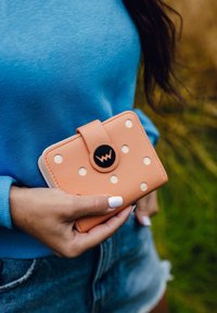 Peach-colored wallet with white polka dots, rectangular shape, featuring a black circular button closure and textured leather material.