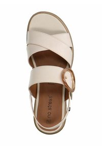 Light beige sandal with crossed strap design, large circular accent, and memory foam insole. Tan footbed and rubber outsole.