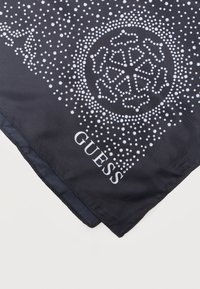 Μαύρο ύφασμα με λευκό διακοσμητικό κυκλικό μοτίβο που μοιάζει με μάνταλα και το όνομα της μάρκας "GUESS" τυπωμένο κοντά στην άκρη.