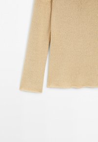 Maglione beige a maniche lunghe lavorato a maglia con dettaglio orlo smerlato su sfondo bianco.