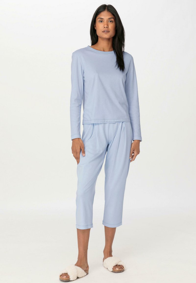 Hellblaues Langarmoberteil und passende, kurze Hose aus weichem Stoff. Mit Rundhalsausschnitt und lockerer Passform. Kombiniert mit flauschigen weißen Sandalen.