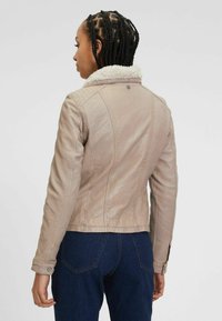 Beige leren jack met een gestructureerde afwerking, voorzien van een witte schapenleren kraag, een getailleerde snit en knoopsluitingen bij de mouwen.