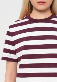 Camiseta a rayas color marrón y blanco, de material de algodón, de mangas cortas, con cuello redondo y detalles de costura visibles.