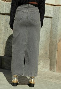 Gray denim maxi skirt with a center back slit and two rear pockets, paired with metallic gold heeled boots featuring decorative accents.