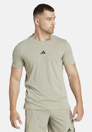 Beige Sport-T-Shirt mit kurzen Ärmeln, Rundhalsausschnitt, mit schwarzem Adidas-Logo auf der Brust, aus leichtem, atmungsaktivem Stoff.