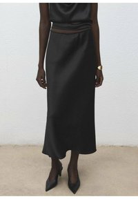Jupe midi en satin noir à texture lisse, silhouette légèrement évasée subtile et taille ajustée, associée à des escarpins noirs pointus.
