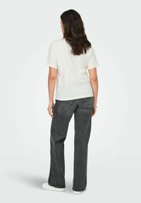 Hvid kortærmet t-shirt, afslappet pasform, parret med højtaljede grå jeans. Teksturen er glat med et svagt marmorering mønster i denim.