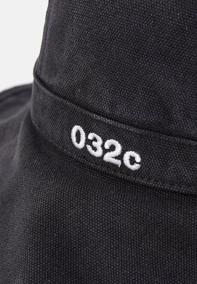 Crni platneni šešir u obliku kante s teksturiranom površinom i bijelim vezom "032c" na vrpci. Simple dizajn s mekim osjećajem.