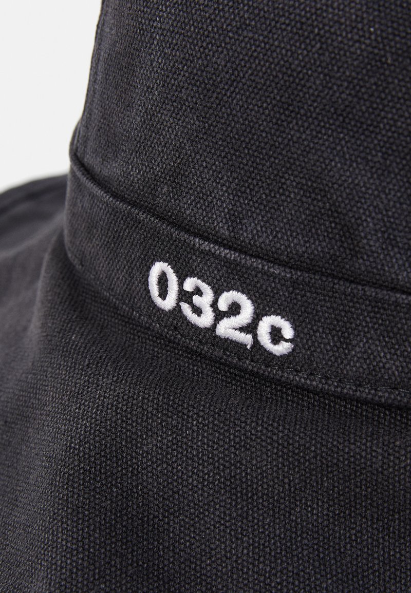 Black fabric bucket hat featuring a textured surface and a white embroidered logo "032c" on the band. Simple design with a soft feel.