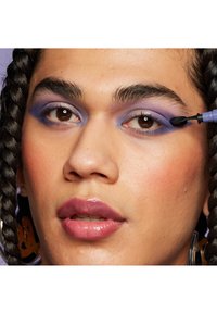 Nahaufnahme eines Gesichts mit lila Lidschatten, der von hell zu dunkel verblendet ist, glänzenden Lippen und geflochtenem Haar. Zeigt eine detaillierte Anwendung des Augen-Make-ups.