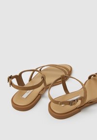 Sandalias de ante marrón con suela de goma plana, que presentan múltiples tiras finas y un cierre de hebilla. La plantilla es beige y suave.