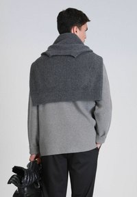 Grijze geribbelde trui met een brede, omgeslagen kraag. De persoon houdt een zwarte, fluffy jas vast. Het materiaal lijkt zacht en textuurrijk.